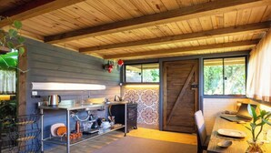 A compact kitchen with a wooden ceiling, a built-in sink, and a small dining area with a table and chairs. - Chalé em Garuva com Vista para a Montanha (Garuva)