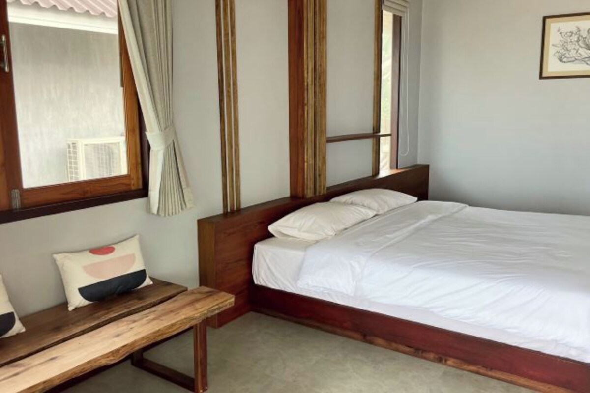 A bedroom with a wooden bed frame, white bedding, a wooden bench, and a window with curtains.