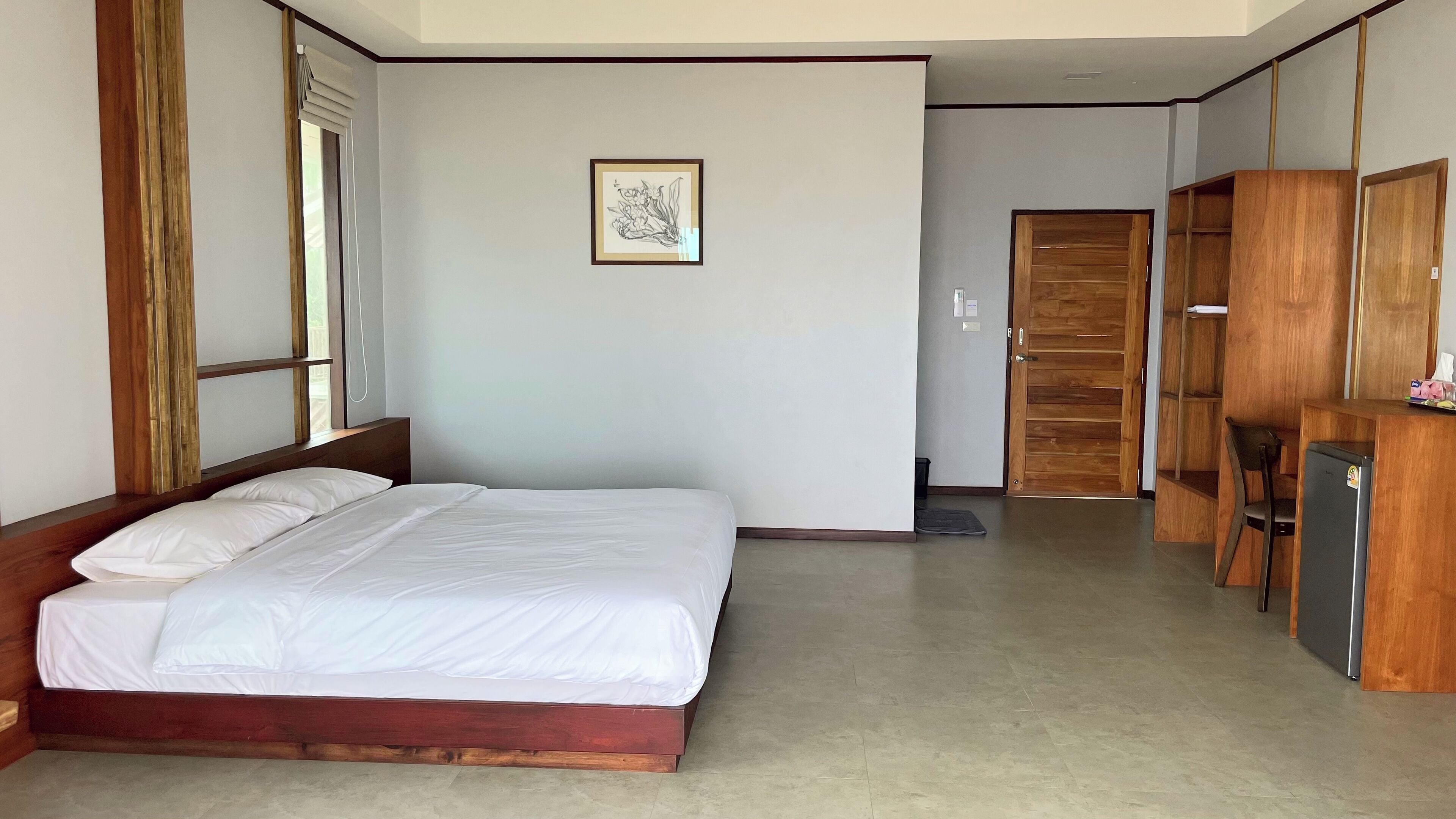 A hotel room with a wooden bed, a small desk, a refrigerator, and a wardrobe.