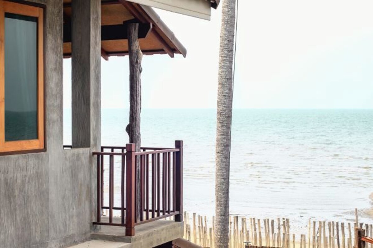 A coastal building with a balcony overlooking the sea, a wooden fence, and a concrete wall.