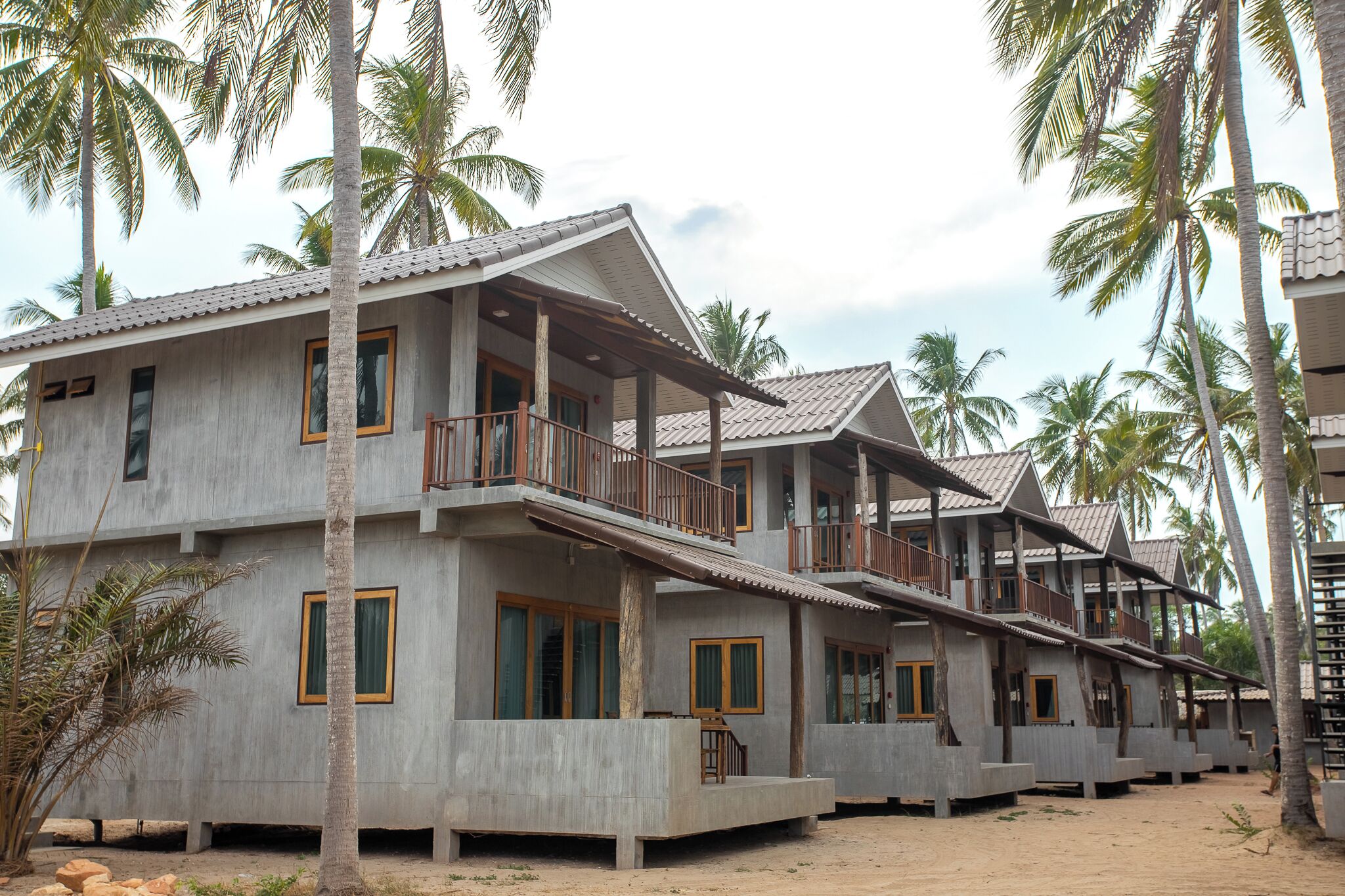 A row of concrete buildings with balconies, surrounded by palm trees.