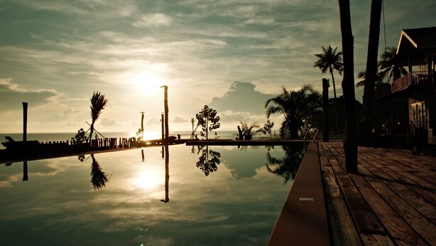 A wooden deck with a pool reflecting palm trees and the sunset. - Laemsui Beach (Chaiya)