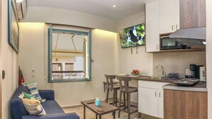 A compact living space with a sofa, a small dining table, a kitchen area with a microwave and sink, and a TV mounted on the wall. - Amara Porto Living | Apartment 1 (Chania)