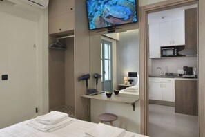A hotel room with a bed, a TV, a mirror, a small table with a hairdryer, and a kitchenette.