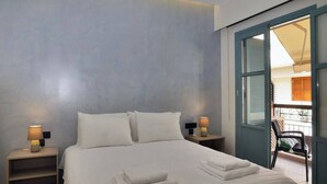 A bedroom with a bed, two bedside tables with lamps, a window with a view of the outside, and a chair by the window. - Amara Porto Living | Apartment 1 (Chania)
