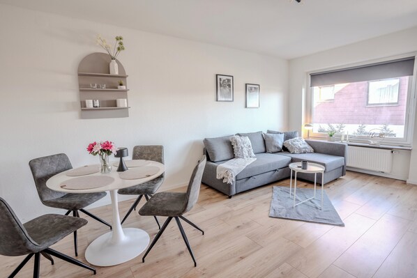 A modern living room with a grey sofa, a round dining table with chairs, and a small side table.