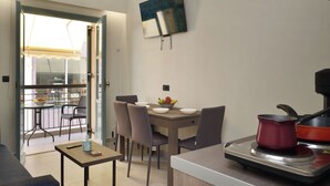 A modern kitchen with a dining area, a TV mounted on the wall, and a balcony with outdoor furniture. - Amara Porto Living | Apartment 2 (Chania)