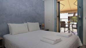 A bedroom with a bed, pillows, a nightstand, a lamp, and a view of an outdoor seating area with chairs and a table. - Amara Porto Living | Apartment 2 (Chania)