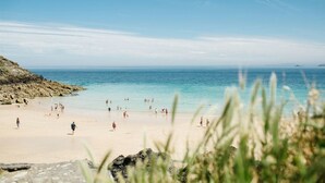 Ein Strand mit Menschen, die am Sand entlanggehen, und das Meer im Hintergrund.
