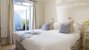 Ein Schlafzimmer mit einem großen Bett, gestreifter Bettwäsche, einem Nachttisch mit Blumen und Blick ins Freie.