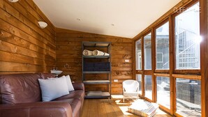 Ein gemütliches Blockhaus-Interieur mit Holzvertäfelung, einem Ledersofa, einem Bücherregal und einem Fenster mit Blick auf ein Gebäude.