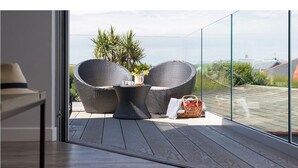 Ein Balkon mit Korbmöbeln, einem kleinen Tisch und einem Korb.