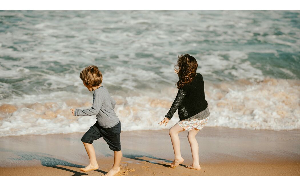 Two children playing on a sandy beach with waves in the background.