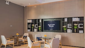 A modern hotel lobby with a reception desk, seating area, and a large screen displaying the hotel name.