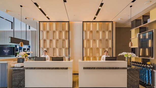 A modern hotel reception area with two reception desks, a large flat-screen TV, and a wall-mounted light fixture.