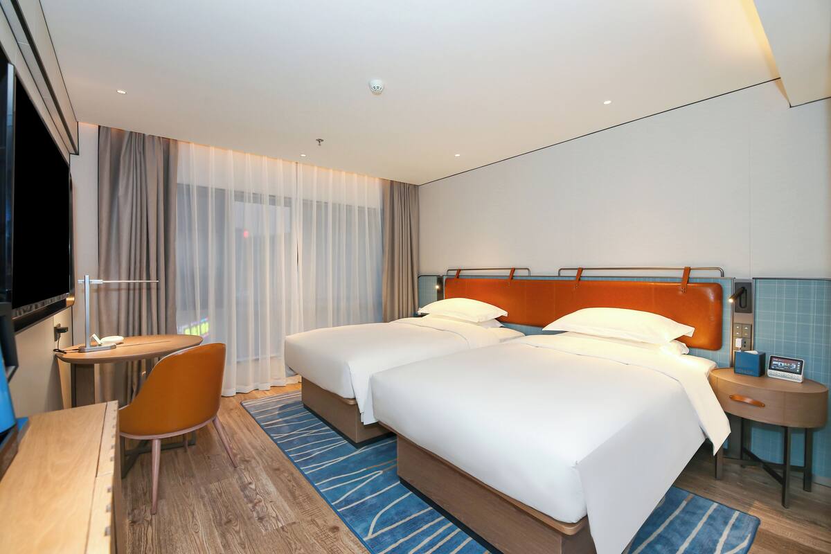 A hotel room with two beds, a desk, a chair, a TV, and a bathroom.