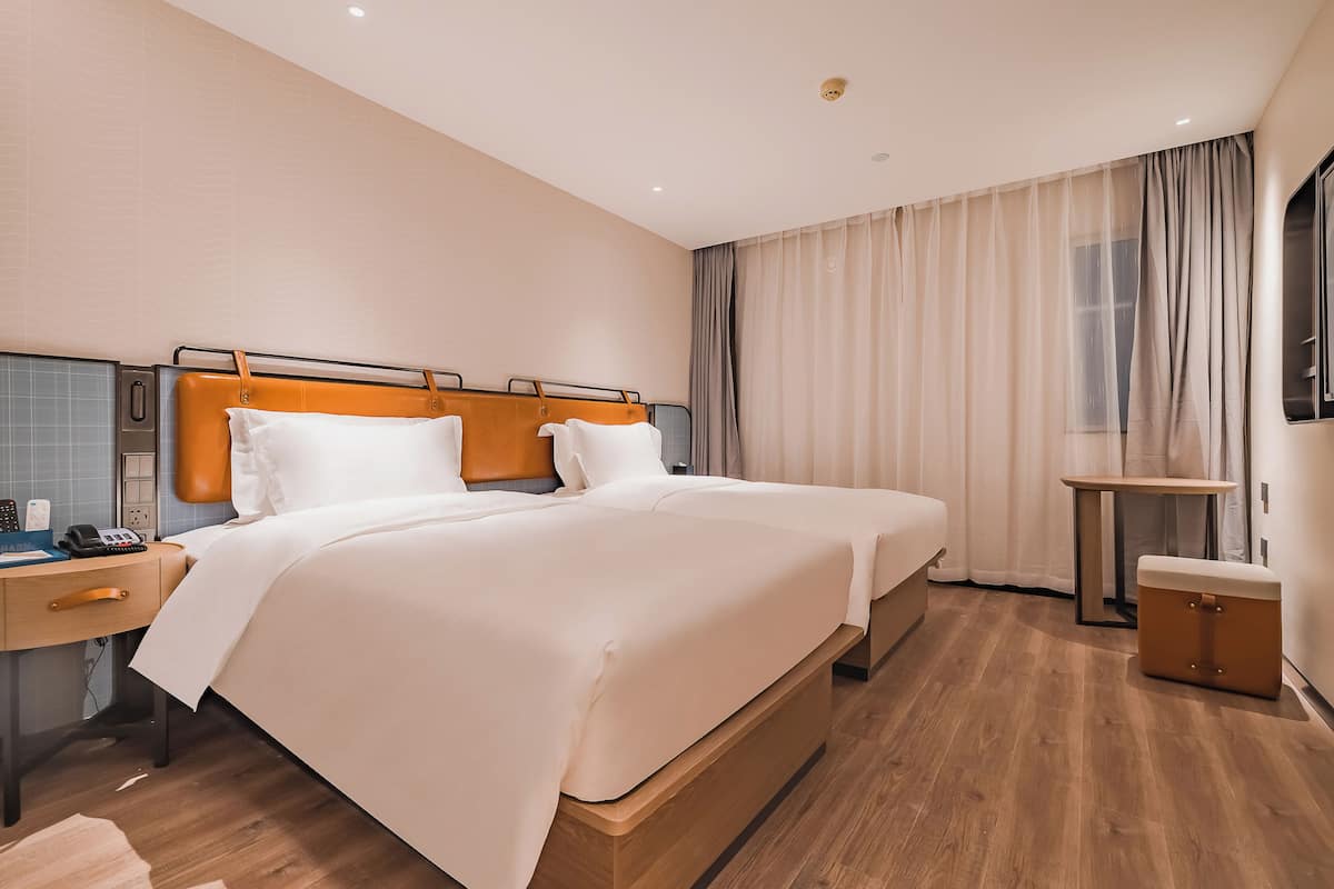 A hotel room with two beds, a bedside table with a phone, a small table, and a suitcase.