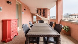 Uma varanda com mesa e cadeiras de jantar, um aparador vermelho e uma escadaria que leva a um andar superior.