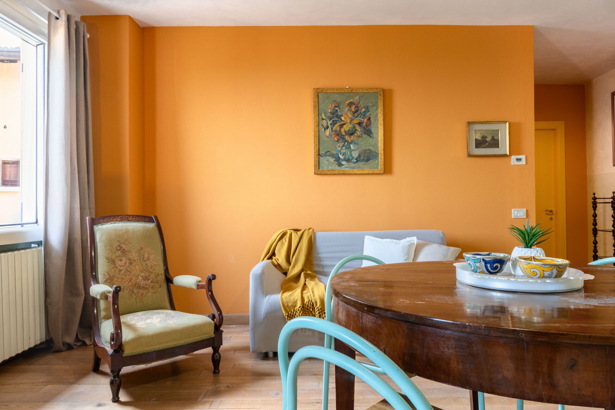 A dining area with a wooden table, a floral armchair, and a sofa with a yellow blanket.