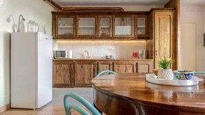 Een keuken met houten kastjes, een witte koelkast en een houten eettafel met stoelen.
