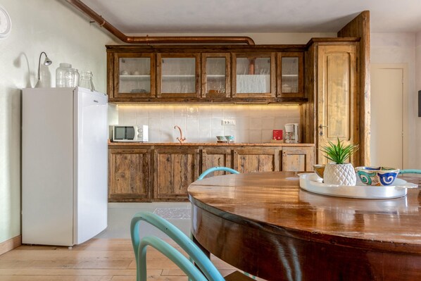 A kitchen with wooden cabinets, a white refrigerator, and a wooden dining table with chairs. - Borgo al Sole 1 by Wonderful Italy (Puegnago del Garda)