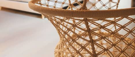 Una silla colgante de macramé en una habitación con una cama y una mesita de noche.