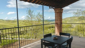 Un balcón con mesa y sillas, con vistas a un paisaje verde con colinas.