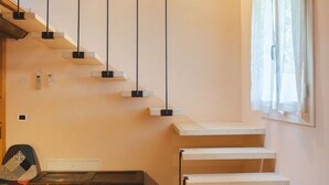 Una escalera con escalones de madera y barandillas negras, un escritorio de madera, y una silla en una habitación con suelo de madera y una ventana con cortinas.
