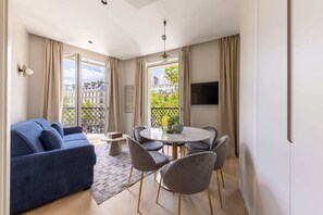 A modern living room with a blue sofa, a round dining table with chairs, and a TV mounted on the wall. - Marais - 2 Bedrooms 2 Living rooms in Paris (Paris)