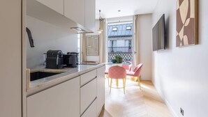 Eine moderne Küche mit Einbauofen, Kaffeemaschine und Spüle. Ein Essbereich mit Tisch und Stühlen sowie ein Balkon mit Blick auf Gebäude.