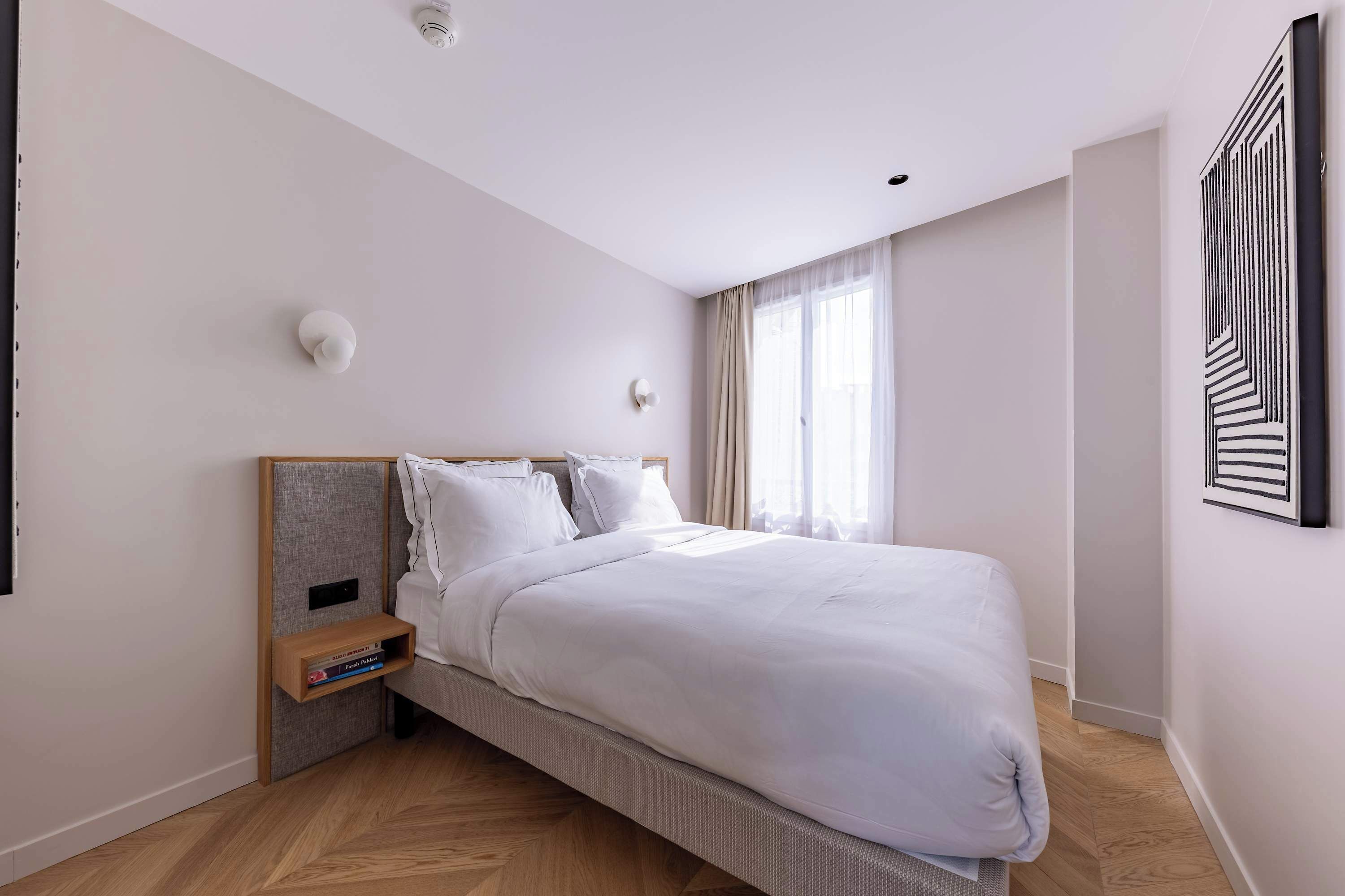 Een moderne slaapkamer met een groot bed, een nachtkastje met boeken en een kunstwerk aan de muur.