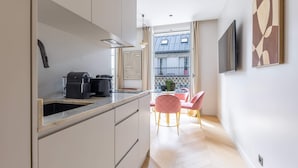 A modern kitchen with a built-in oven, a coffee machine, and a sink. There is a dining area with a table and chairs, and a balcony with a view of buildings.