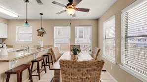 A kitchen with a dining area, featuring a ceiling fan, pendant lights, and a large window with blinds.