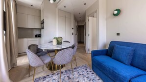 A modern living room with a blue sofa, a round dining table with four chairs, and a kitchen area with white cabinets and a marble countertop. - Marais - 2 Bedrooms in Paris (Paris)