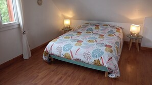 Ein Schlafzimmer mit einem Bett, zwei Nachttischen mit Lampen, einem Fenster mit Vorhängen und einem Holzboden.