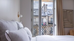 Una habitación de hotel con una cama, un ventanal con vista a edificios y una puerta.