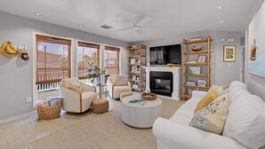 A modern living room with a fireplace, white sofas, a coffee table, and a bookshelf. - Pirate's Beach Retreat! A short walk to the beach. (Galveston)