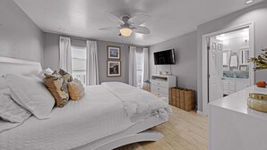 A bedroom with a bed, a ceiling fan, a TV, a dresser, and a bathroom visible through an open door. - Pirate's Beach Retreat! A short walk to the beach. (Galveston)