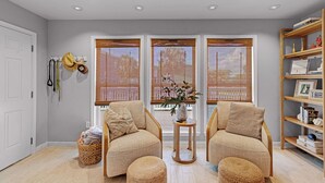 A room with two armchairs, a small table with a vase, a bookshelf, and a window with blinds. - Pirate's Beach Retreat! A short walk to the beach. (Galveston)