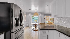 A modern kitchen with a large stainless steel refrigerator, white cabinetry, and a dining area with a round table and chairs. - Pirate's Beach Retreat! A short walk to the beach. (Galveston)