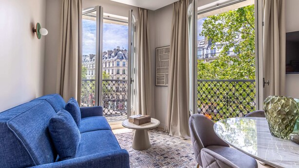 A modern living room with a blue sofa, a round coffee table, and a view of the city through large windows. - Marais - 2 Bedrooms 2 Living rooms in Paris (Paris)