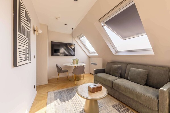 A modern living room with a sofa, a round coffee table, a TV, and a dining area with chairs and a table.