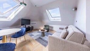 Un salon moderne doté d’un plafond haut, de fenêtres de toit, d’un téléviseur à écran plat, d’une table à manger avec des chaises et d’un canapé.