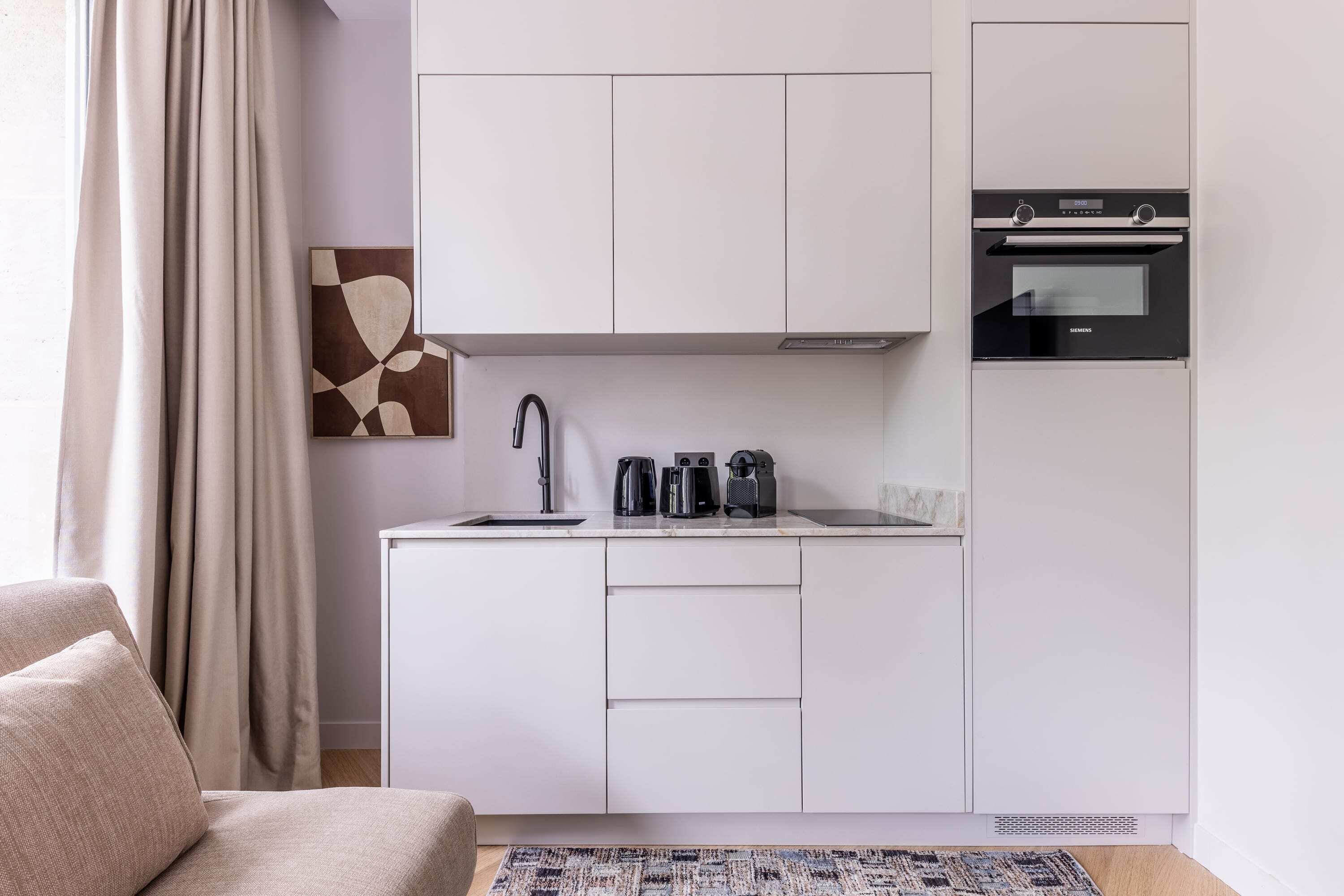 A compact kitchen with white cabinets, a built-in oven, and a coffee maker on the countertop.