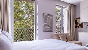A hotel room with a large bed, a sofa, a window with a view of trees, and a wall-mounted artwork. - Marais - Studio in Paris (Paris)
