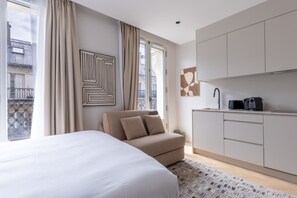 A modern hotel room with a large bed, a sofa, a kitchen area, and a view of the city. - Marais - Studio for 3 in Paris (Paris)