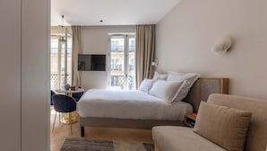 A modern hotel room with a bed, a sofa, a TV, and a balcony view.