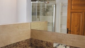 Un baño con lavamanos blanco, un espejo, ducha y puerta de madera.