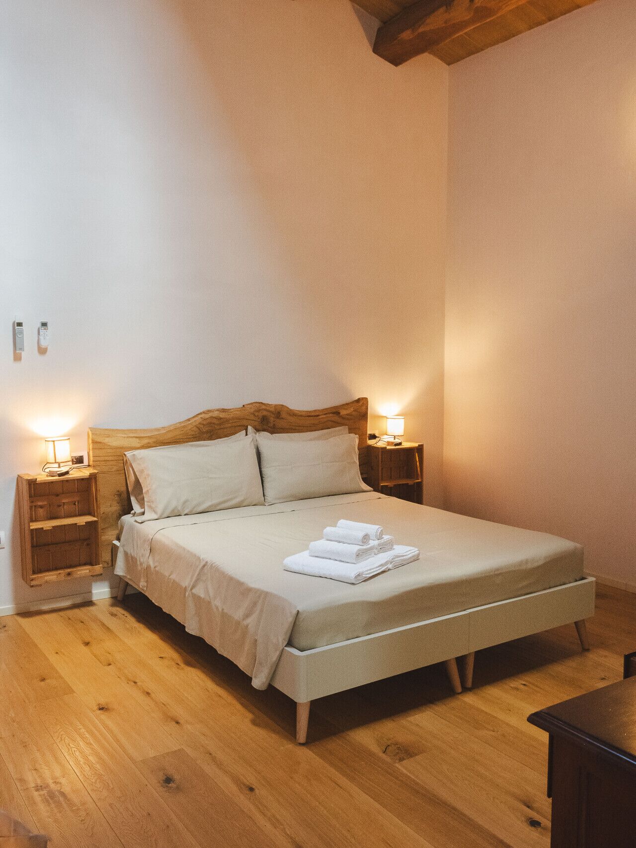 Quarto com cabeceira de madeira, mesa de cabeceira de madeira com abajur e mesinha de cabeceira com lâmpada.