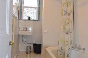 A bathroom with a white sink, a window with a stained glass design, a bathtub, and a shower curtain with a sea creature pattern. - Beach front house (Wellington)